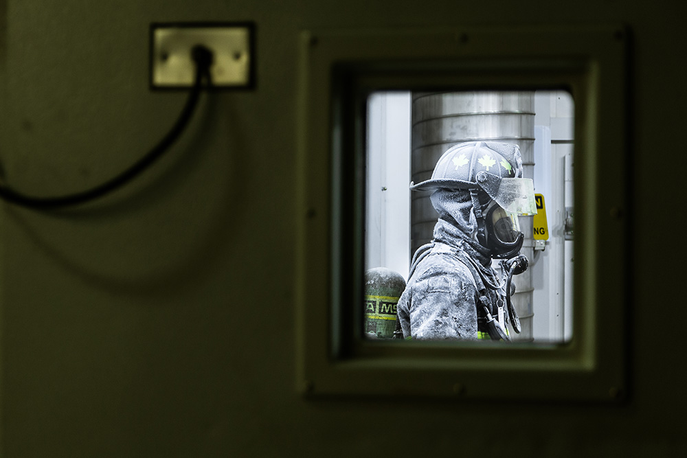 A firefighter undergoing rigorous testing inside ACE at Ontario Tech University, in a controlled environment, fully equipped with protective gear and a self-contained breathing apparatus. This scenario at ACE is part of a typical training exercise to ensure readiness, physical/mental resiliency, and firefighting operations in adverse conditions.